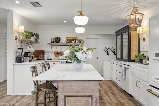 kitchen featuring white cabinetry, decorative light fixtures, a center island, light stone countertops, and hardwood / wood-style floors