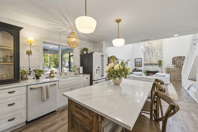 kitchen featuring hanging light fixtures, white dishwasher, light stone countertops, white cabinets, and high end refrigerator