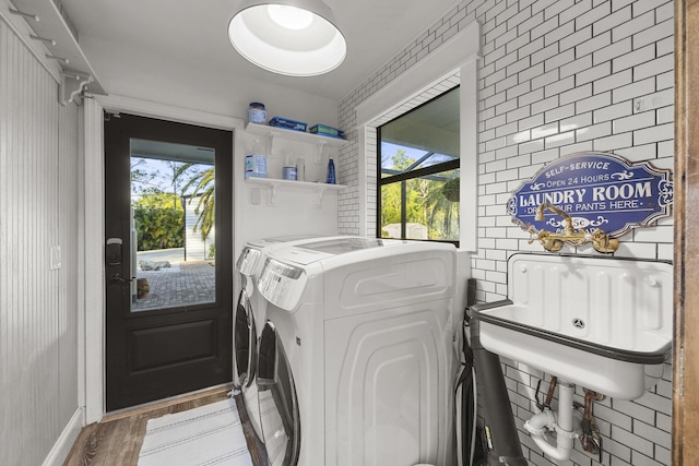 washroom featuring separate washer and dryer, hardwood / wood-style floors, and brick wall