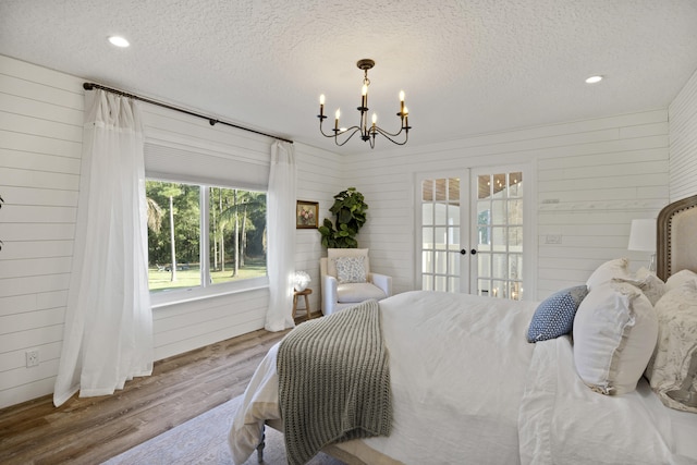 bedroom featuring hardwood / wood-style flooring, an inviting chandelier, wooden walls, a textured ceiling, and french doors