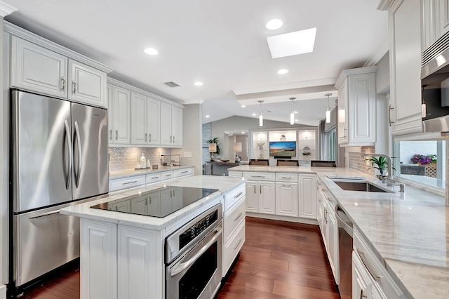 kitchen featuring hanging light fixtures, kitchen peninsula, stainless steel appliances, vaulted ceiling with skylight, and white cabinets