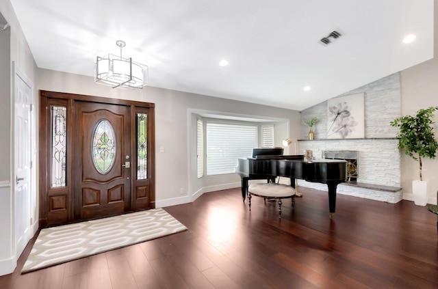 entryway featuring dark wood-type flooring, an inviting chandelier, a fireplace, and vaulted ceiling