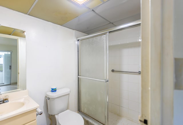 bathroom with vanity, toilet, an enclosed shower, and a drop ceiling