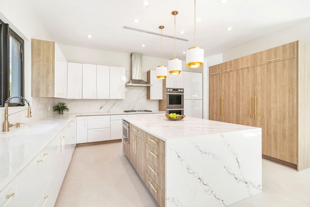 kitchen with wall chimney range hood, sink, hanging light fixtures, white cabinets, and a kitchen island