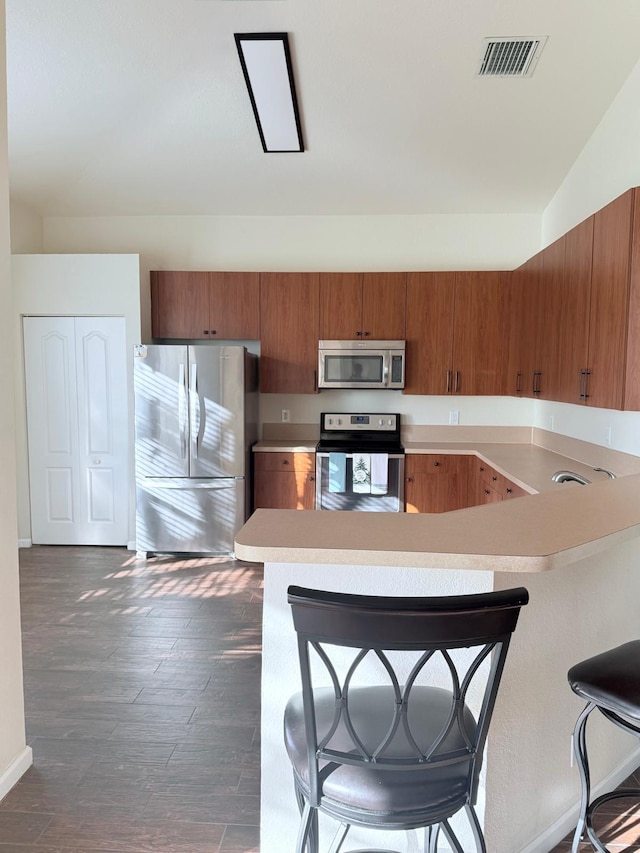 kitchen featuring stainless steel appliances, dark hardwood / wood-style flooring, a breakfast bar, and kitchen peninsula