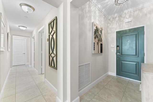 hallway with light tile patterned floors, a textured ceiling, visible vents, and baseboards