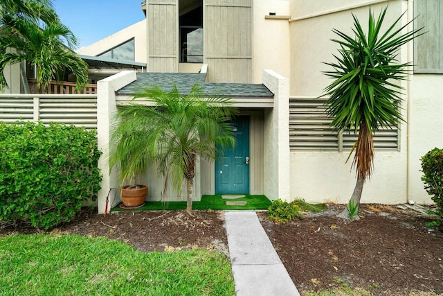 doorway to property with a shingled roof, fence, and stucco siding