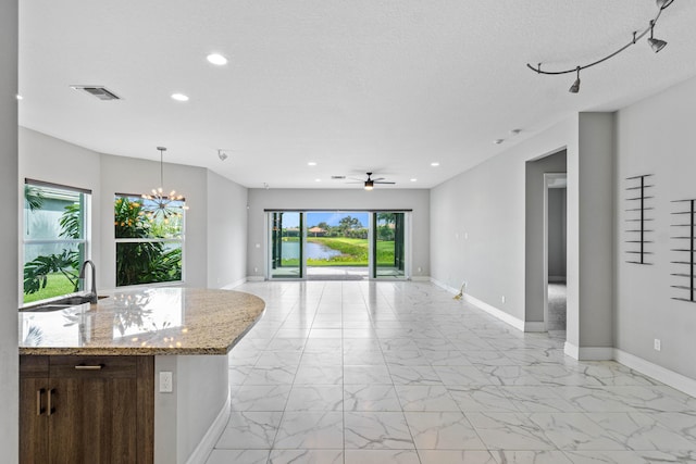 kitchen featuring light stone counters, sink, hanging light fixtures, and a textured ceiling