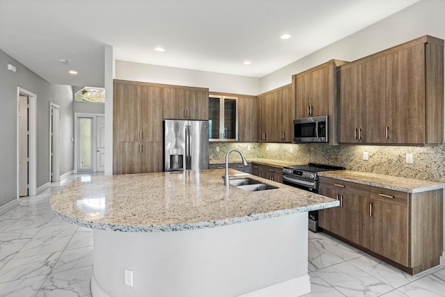 kitchen featuring sink, appliances with stainless steel finishes, light stone counters, a center island with sink, and decorative backsplash