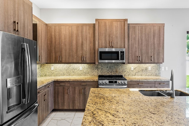 kitchen featuring stainless steel appliances, sink, light stone counters, and decorative backsplash