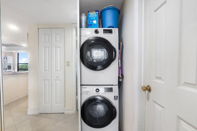 clothes washing area with stacked washer and clothes dryer, light tile patterned floors, and laundry area