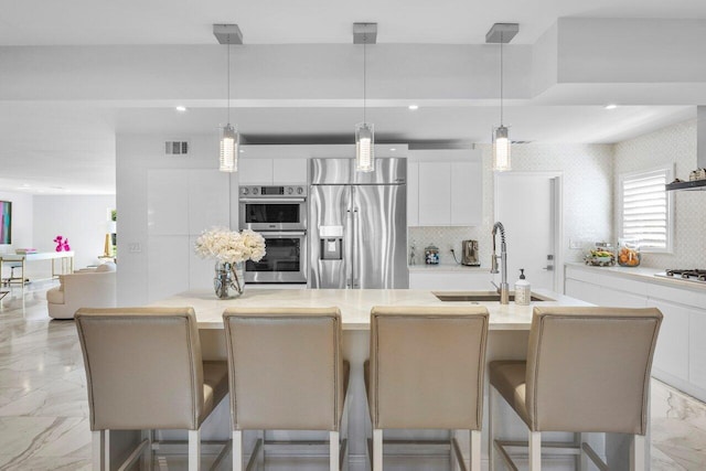 kitchen with visible vents, marble finish floor, a center island with sink, a sink, and appliances with stainless steel finishes