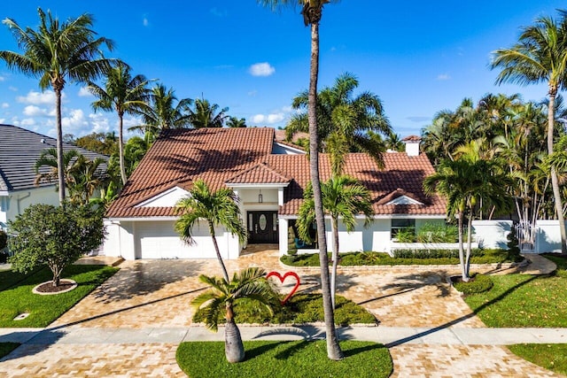 mediterranean / spanish home featuring stucco siding, a tile roof, decorative driveway, fence, and a garage