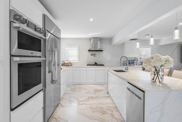 kitchen featuring marble finish floor, modern cabinets, a sink, appliances with stainless steel finishes, and wall chimney exhaust hood