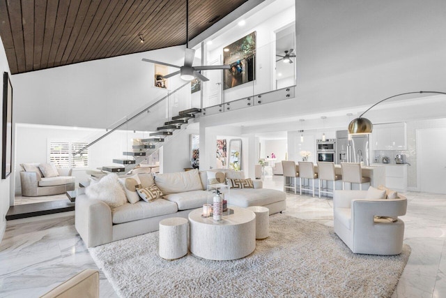 living area featuring marble finish floor, a high ceiling, wooden ceiling, ceiling fan, and stairs