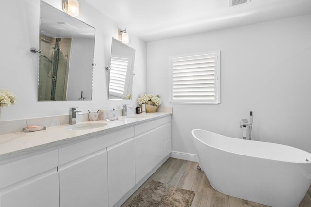 bathroom featuring wood finished floors, a soaking tub, double vanity, a sink, and a shower stall