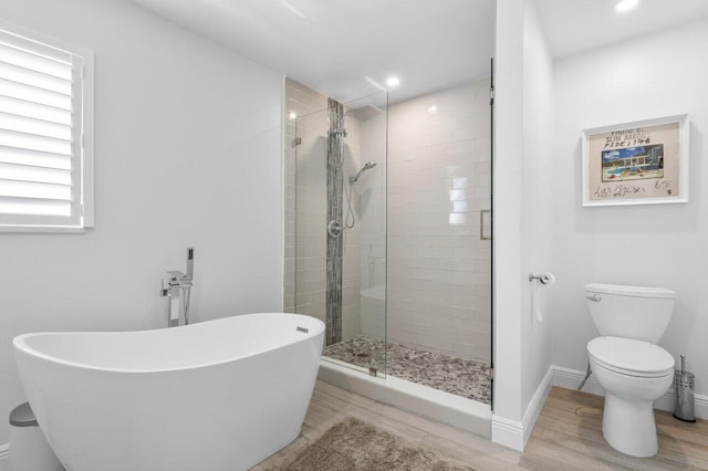 full bath with wood finished floors, baseboards, a freestanding tub, a stall shower, and toilet