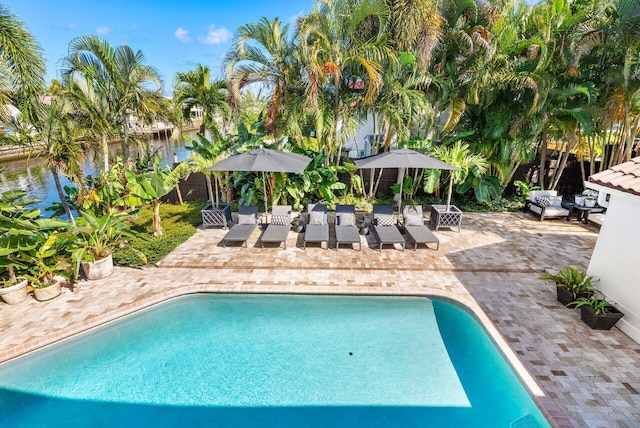pool with a water view, fence, and a patio area