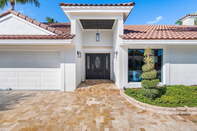 entrance to property featuring stucco siding, driveway, an attached garage, and a tiled roof