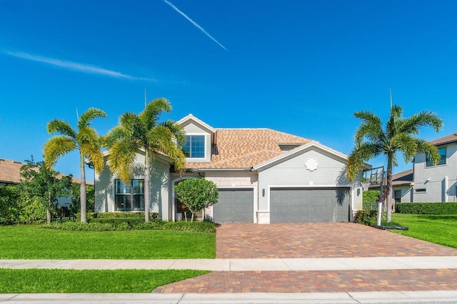 mediterranean / spanish house featuring an attached garage, a tiled roof, decorative driveway, stucco siding, and a front lawn