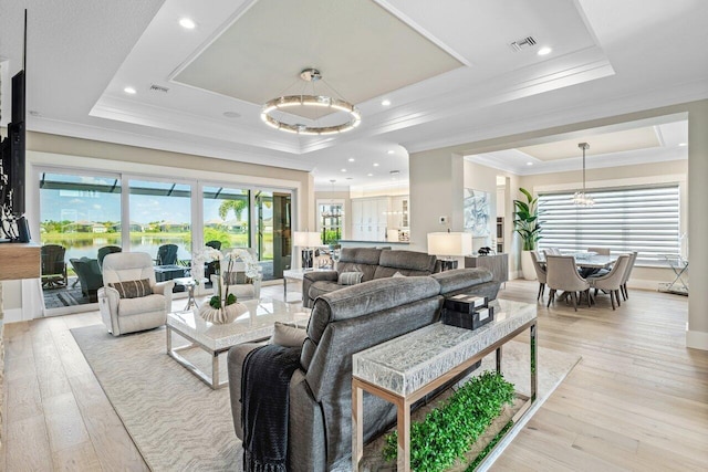 living room with light wood finished floors, visible vents, a raised ceiling, and ornamental molding