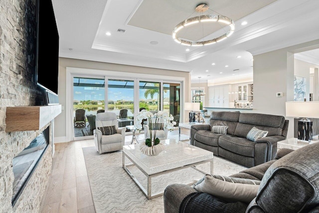 living room with visible vents, light wood-style flooring, a fireplace, crown molding, and a raised ceiling