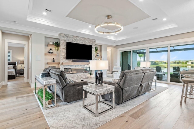 living room featuring light wood-type flooring, visible vents, a raised ceiling, and crown molding