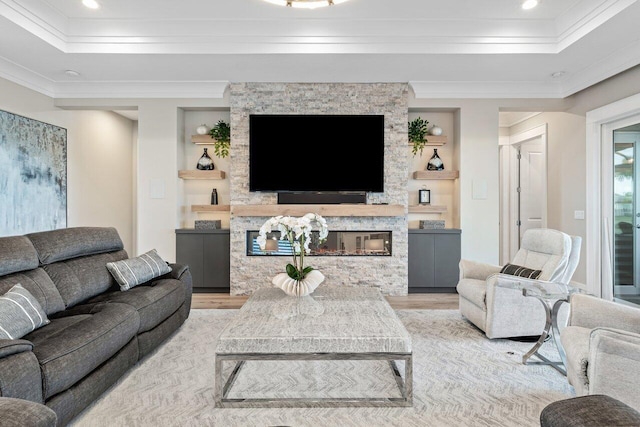 living area with a raised ceiling, light wood-style flooring, a fireplace, and crown molding