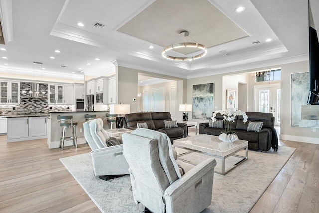 living room with visible vents, light wood-style floors, and a tray ceiling