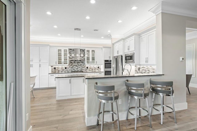 kitchen featuring white cabinetry, stainless steel appliances, a peninsula, light wood finished floors, and glass insert cabinets