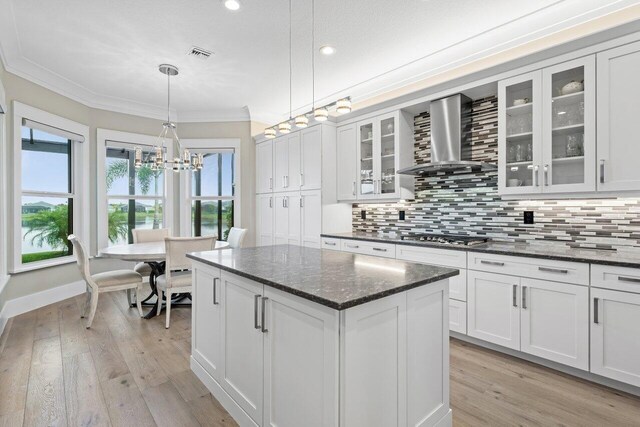 kitchen featuring light wood finished floors, wall chimney exhaust hood, backsplash, and ornamental molding