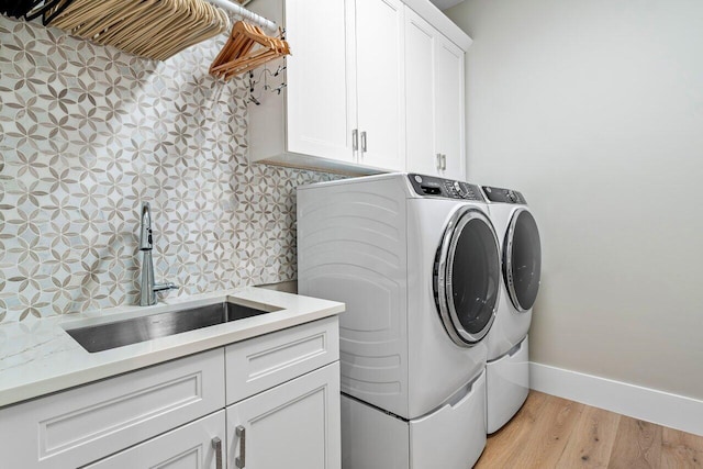 laundry area with washing machine and clothes dryer, light wood finished floors, baseboards, cabinet space, and a sink