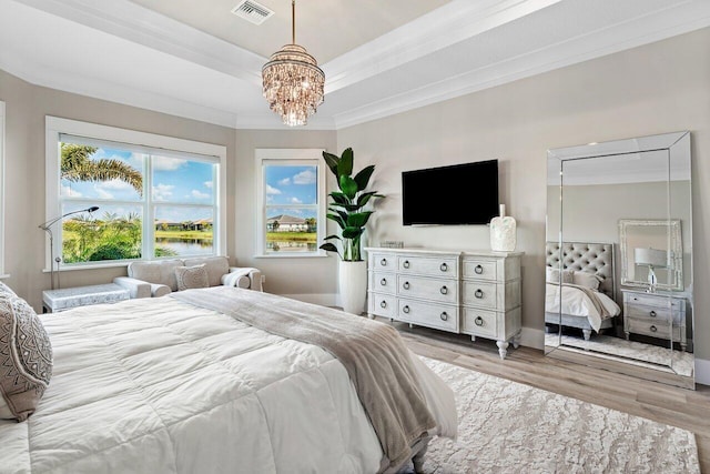 bedroom featuring wood finished floors, visible vents, a tray ceiling, ornamental molding, and a chandelier