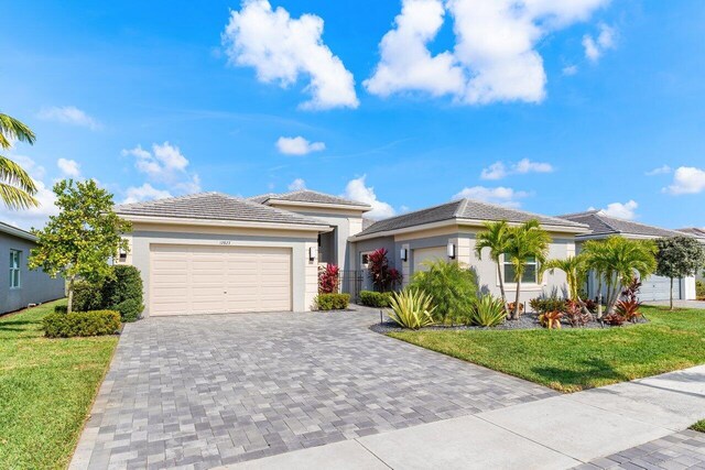 prairie-style home with stucco siding, a front lawn, a garage, a tile roof, and decorative driveway