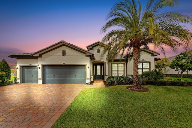 mediterranean / spanish home featuring decorative driveway, a yard, stucco siding, an attached garage, and a tiled roof