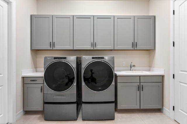 clothes washing area with light tile patterned floors, washing machine and dryer, a sink, baseboards, and cabinet space