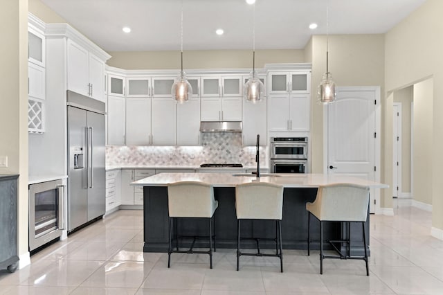 kitchen featuring appliances with stainless steel finishes, a kitchen island with sink, light countertops, and glass insert cabinets