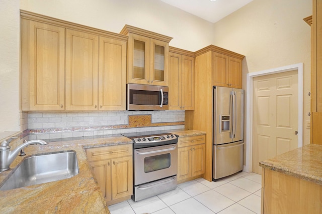 kitchen featuring light stone counters, tasteful backsplash, appliances with stainless steel finishes, glass insert cabinets, and a sink