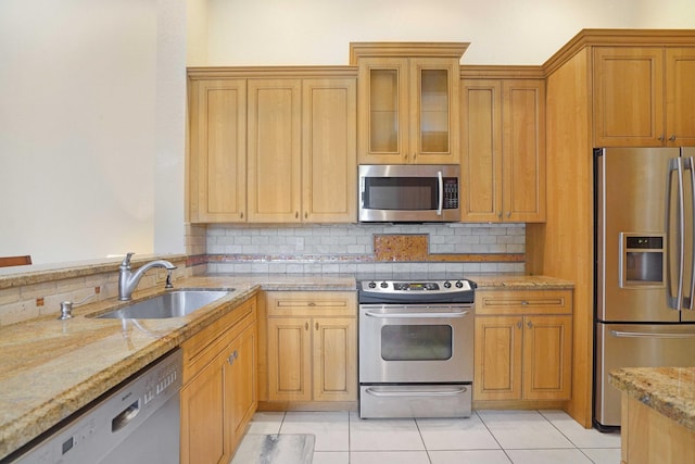 kitchen featuring stainless steel appliances, backsplash, glass insert cabinets, a sink, and light stone countertops