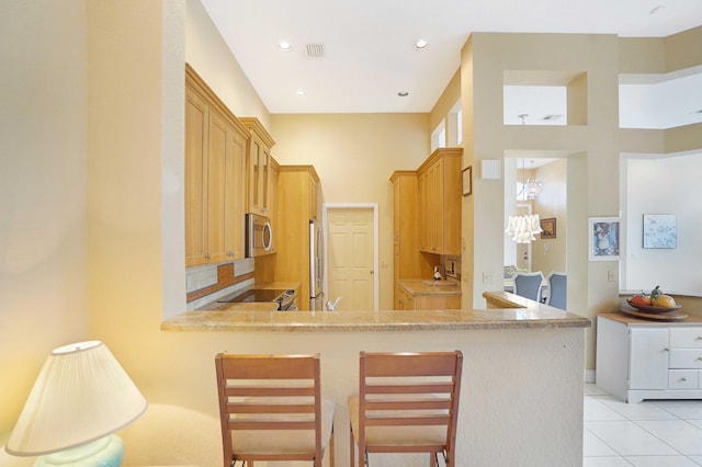 kitchen featuring light tile patterned floors, appliances with stainless steel finishes, a breakfast bar area, a peninsula, and light countertops