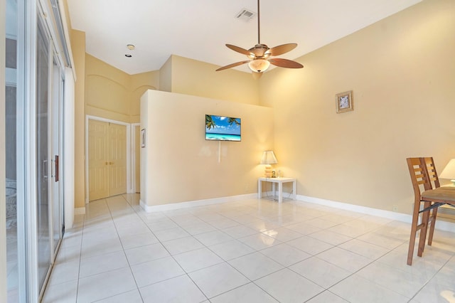 empty room featuring light tile patterned floors, visible vents, a high ceiling, a ceiling fan, and baseboards