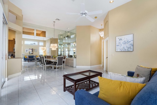 living room with ceiling fan with notable chandelier, a high ceiling, light tile patterned flooring, and baseboards