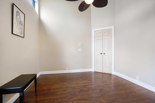 spare room with dark wood-style flooring, a high ceiling, ceiling fan, and baseboards