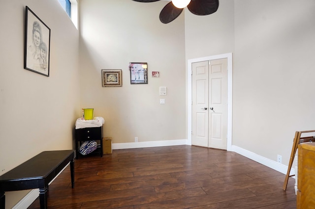 interior space with a towering ceiling, dark wood-style floors, ceiling fan, and baseboards