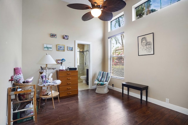 living area with ceiling fan, dark wood-type flooring, a towering ceiling, and baseboards