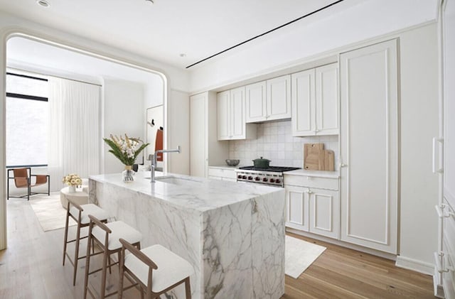 kitchen featuring light stone countertops, white cabinets, a sink, and light wood finished floors