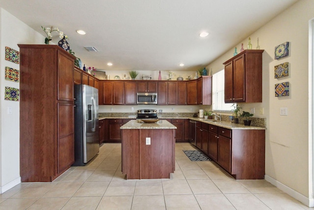 kitchen with a kitchen island, sink, light tile patterned floors, stainless steel appliances, and light stone countertops