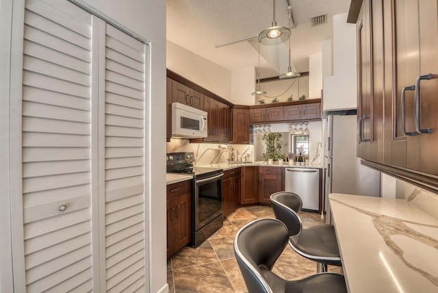 kitchen with stainless steel appliances, light stone counters, a textured ceiling, and decorative backsplash