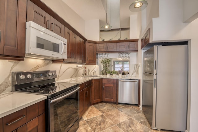 kitchen featuring stainless steel appliances, light countertops, a sink, light stone finish floors, and tasteful backsplash