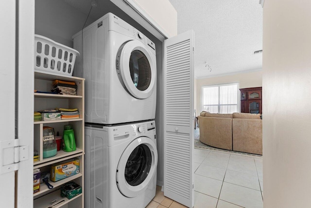 laundry area featuring stacked washer and dryer, crown molding, light tile patterned floors, and a textured ceiling